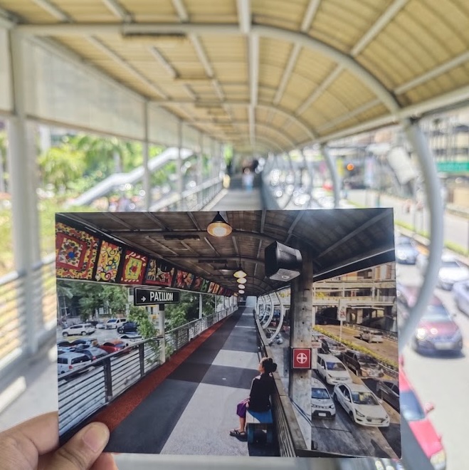 Person holding a photo of the place in the background which is slightly different
