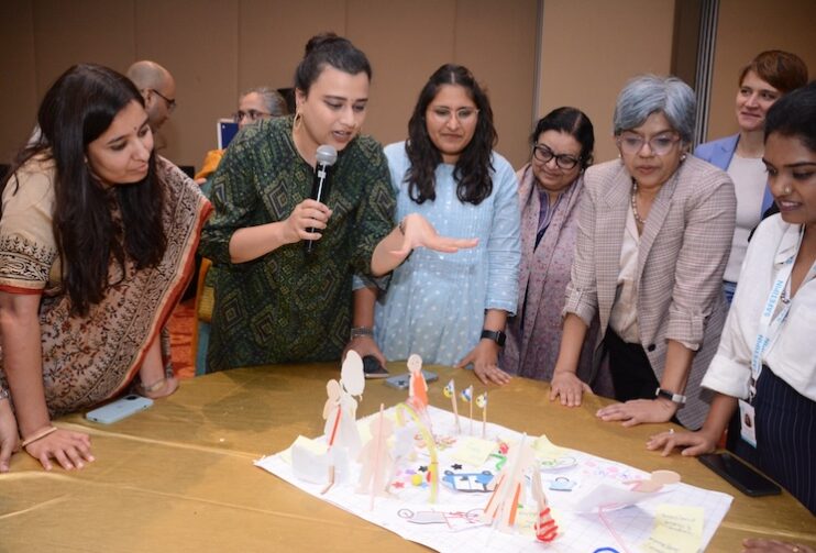 women standing around a table talking about a crafted model